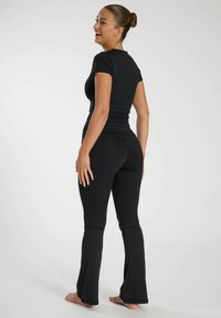 Svart åtsittande t-shirt och utsvängda leggings i elastiskt tyg. Outfiten är sömlös, med en slät yta och inga synliga mönster.