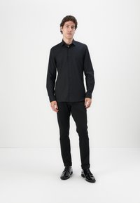 Svart långärmad skjorta med knäppning fram, slim fit och slät struktur, kombinerat med svarta slim-fit byxor och polerade skor.