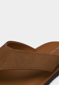 Καφέ σανδάλι με πλεκτό υφασμάτινο λουράκι και ταμπά πέλμα, με τακτοποιημένα ράμματα και μαύρο χείλος σόλας.