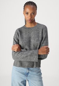 Pull en maille gris avec un col rond, texture côtelée, épaules tombantes et coupe courte, associé à un jean bleu clair.
