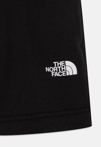 Juodas medvilnės audinys, kuriame matomas baltas siuvinėtas logotipas su pusmėnulio dizainu ir tekstu "THE NORTH FACE". Įtrauktas matomas siuvimo detalės.