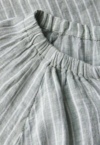 Tessuto di lino verde chiaro con sottili strisce verticali bianche. Il collo presenta dettagli arricciati, che aggiungono texture al design.