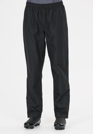 Schwarze wasserdichte Hose mit elastischem Bund, getragen über schwarzen Golfschuhen an einer Person vor einfachem Hintergrund.