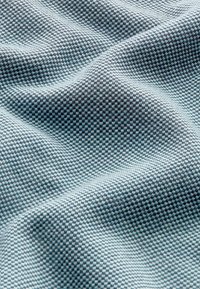 Tissu texturé bleu clair et gris, présentant un motif en grille qui crée de la profondeur avec des nuances variées et des plis doux.