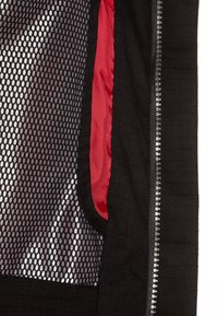 Veste noire avec panneaux en mesh et une doublure rouge vive. Tissu texturé avec une fermeture éclair latérale.