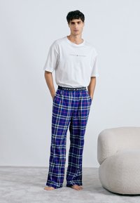 Biela bavlnená tričko s logom "Tommy Hilfiger", kombinované s modrými kockovanými pyžamovými nohavicami so žltými a bielymi pruhmi, elastickým pásom.