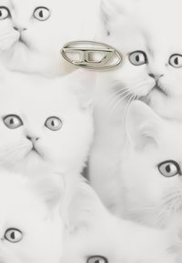Visages de chats blancs avec des yeux bleus imprimés sur une surface, présentant une épingle en métal argenté de forme ovale et de design abstrait.