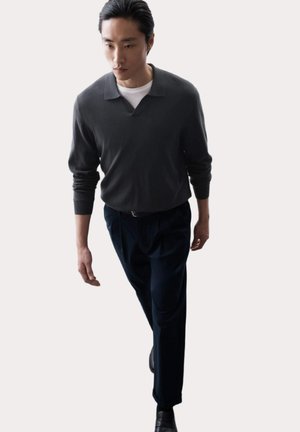 Gray long-sleeve polo with a ribbed collar, paired with navy pleated trousers and black shoes. Smooth texture, minimal design.