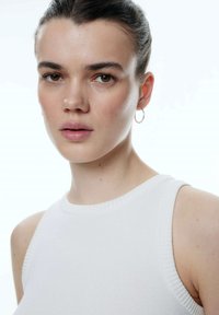 Witte geribde tanktop met een ronde hals, voorzien van een fijn textuur en zonder zichtbare patronen. Kleine ringoorbel in het linkeroor.