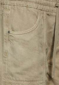 Beige cargo shorts made of textured fabric, featuring an elastic waistband, front pocket with a metal snap, and visible stitching details.