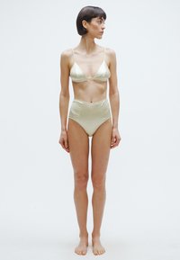 Σετ μαγιό από σατέν σε ανοιχτό πράσινο χρώμα, δύο κομματιών. Το πάνω μέρος έχει τριγωνικά cups και λεπτές τιράντες· το κάτω μέρος με ψηλή μέση και λεία υφή.