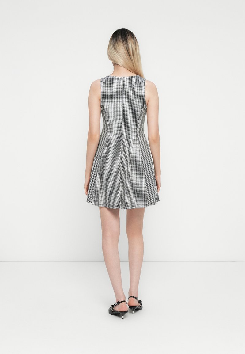 Robe à carreaux noir et blanc avec un corsage ajusté et une jupe évasée, dotée d'un col rond et d'un design sans manches. Texture lisse.