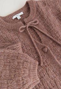 Pull mauve en maille avec motif de feuilles, col et poignets côtelés, bouton en forme de cœur et nœud noué au niveau de l'encolure.