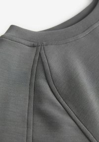 Tissu gris à la texture lisse, avec un col arrondi et des détails de plis subtils, mettant en valeur un design épuré et moderne.