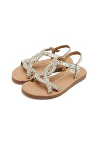 Sandalias planas beige con un diseño de tiras, adornadas con cuentas transparentes y un cierre de hebilla. Presentan una suela texturizada de color marrón claro.