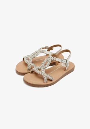 Sandali piatti beige con design a strisce, decorati con perline trasparenti e chiusura a fibbia. Presentano una suola testurizzata di colore marrone chiaro.