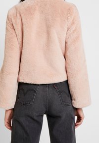 Roze jas van namaakbont met een zachte, gestructureerde oppervlak, een cropped design en brede mouwen, gecombineerd met donkere spijkerbroek met achterzakken.