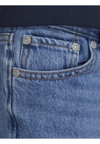 Jeans av denim i ljusblå färg, med synlig sömnad och två metallnitar på fickan. Texturen är slät med en klassisk passform.