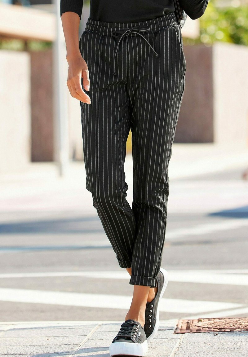 Czarno-białe paskowane zwężane spodnie z elastycznym pasem i sznurkiem, w połączeniu z czarnymi sneakersami i podwiniętymi mankietami.