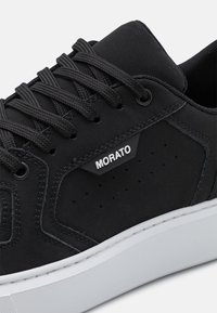 Baskets noires avec de grosses lacets noirs, semelle blanche, panneau latéral perforé et marque "MORATO" sur le côté près des lacets.