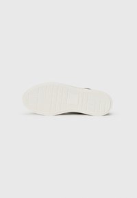 Adidași negri cu o talpă din cauciuc albă, prezentând un model texturat și vârful rotund. Designul tălpii include elemente de tracțiune de tip grilă.