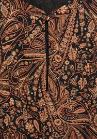 Tissu noir avec un motif cachemire floral orange et marron complexe. Présente un détail d'encolure en forme de trou de serrure et une texture subtile.
