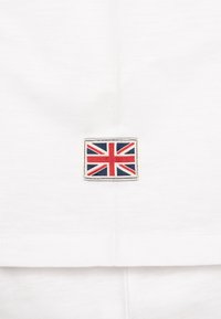 Fehér pamut ing, kis hímzett Union Jack címerrel, téglalap alakú, piros, kék és fehér színekben. Sima textúra.