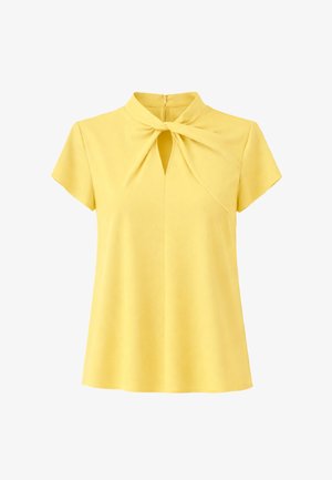 Żółta bluzka z krótkim rękawem z detalem skręconego węzła i wycięciem w kształcie klucza przy dekolcie, z zamkiem błyskawicznym z tyłu.