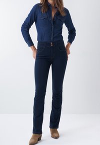 Chemise en denim noir avec des poches poitrine doubles, fermeture à boutons et manches longues. Jean ajusté assorti en noir avec des coutures discrètes et taille haute.