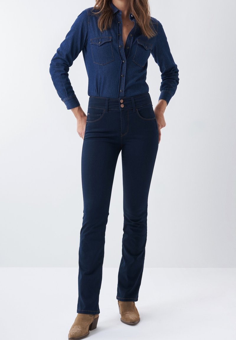 Chemise en denim noir avec des poches poitrine doubles, fermeture à boutons et manches longues. Jean ajusté assorti en noir avec des coutures discrètes et taille haute.