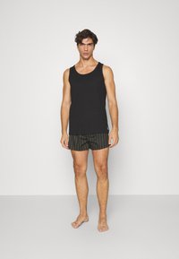 Top sin mangas negro combinado con un bañador a rayas verdes. La tela parece ligera y el estilo es casual. Los bañadores cuentan con una cinturilla elástica.