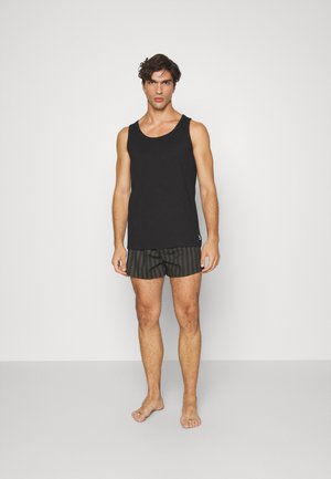 Svart tanktopp kombinert med grønne stripete badebukser. Stoffet ser lett ut, og stilen er uformell. Bukserne har elastisk midje.