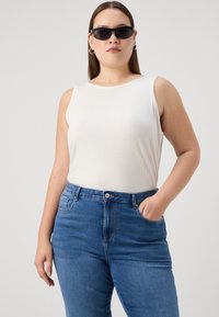 White ribbed tank top paired with blue high-waisted jeans. The model wears black sunglasses and has straight hair. Simple, functional design.