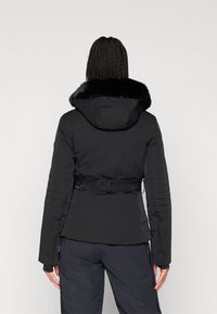 Μαύρο μπουφάν με μόνωση και ψεύτικη γούνα στο γιακά, με ζώνη στη μέση, ριμπ μανίκια και μαλακή υφή, προβαλλόμενο από πίσω.