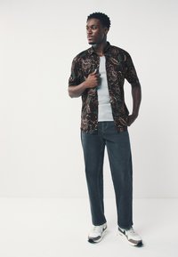 Chemise noire à manches courtes avec motif floral, débardeur gris, jean foncé et baskets blanches avec accents gris. Texture lisse, coupe décontractée.