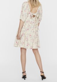 Květinové šaty v krémové barvě, s krátkými nafouknutými rukávy, zapínáním na tkaničku na zádech a sukni ve volánech. Ozdobeny růžovými a modrými květinami.