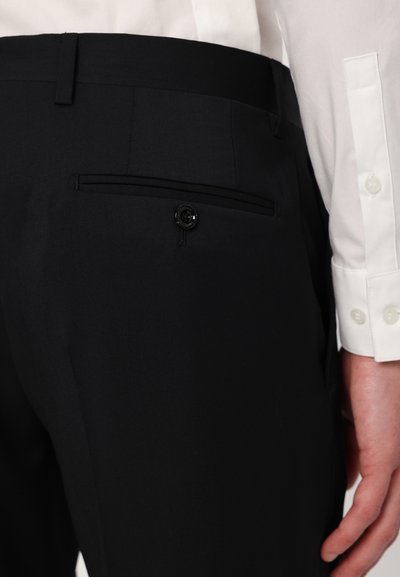 Pantalones negros ajustados que cuentan con un bolsillo trasero con cierre de botón y una tela lisa y texturizada. Acompañados de una camisa de vestir blanca.