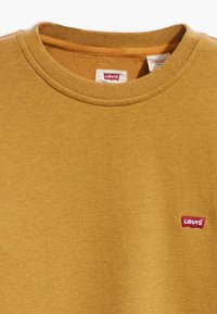 Mosterdgele crew neck sweatshirt met klein rood en wit Levi's logo op de linker borst en bijpassend detail aan de binnenkant van de kraag.