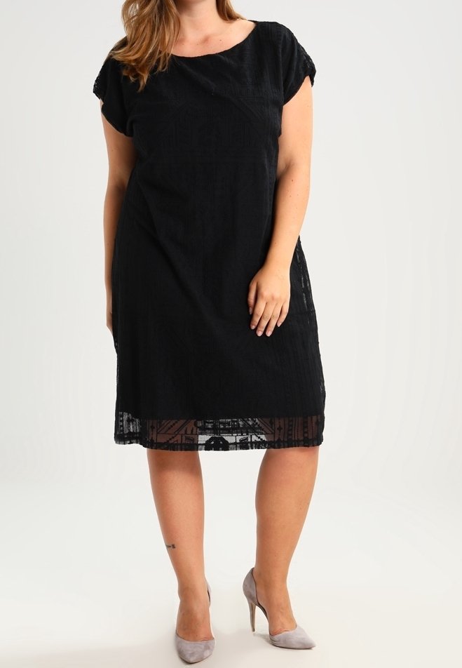 Zwarte jurk met korte mouwen van textuurstof en een patroon aan de zoom, met een losse pasvorm en rechte silhoët. Gecombineerd met lichtgrijze hakken.
