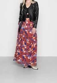 Musta nahkainen lyhyt takki mustan topin päällä, yhdistettynä pitkään, laineilevaan ruosteenväriseen hameeseen, jossa on kukkakuosi sinisen, violetin ja oranssin sävyissä.