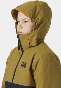 Hnědá a černá kapucňová bunda se zapínáním na zip, vybavená elastickou kapucí a logem na hrudi. Hladký, lehký materiál.