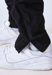 Pantalones negros ajustados con cremalleras en los tobillos combinados con zapatillas blancas. Las zapatillas cuentan con detalles de malla y una suela texturizada.