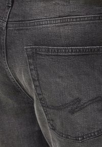 Czarne dżinsy z denimu z teksturowanym wykończeniem, pięcioma kieszeniami oraz wzmocnionymi przeszyciami na kieszeniach. Brak widocznych ozdób.