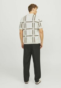 Kortærmet polo-shirt i lys grå med brunt rutemønster, parret med sorte bukser. Materialet ser ud til at være strikket, hvilket giver et tekstureret look.