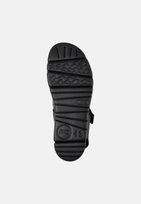 Black sandal sole with textured grooves and patterns. Features a rounded shape and branding embossed in a circular detail. Size 42.