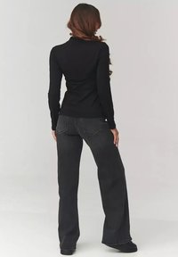 Czarna bluzka z długim rękawem połączona z luźnymi czarnymi dżinsami. Stylizacja wyróżnia się elegancką, dopasowaną sylwetką i miękką teksturą materiału.