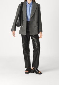 Šedé dvouřadé sako z vlněné směsi přes modrou pruhovanou košili, v kombinaci s černými koženými kalhotami a masivními černými sandály.