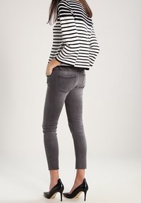 Haut à manches longues à rayures noires et blanches, associé à un jean gris coupe slim et des chaussures à talons noirs. Détail : une poche arrière.