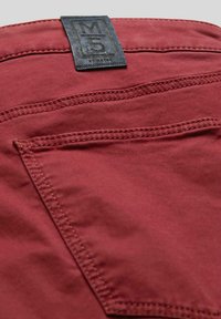 Rote Baumwollhosen mit einem strukturierten schwarzen Etikett, auf dem "M5" auf dem Bund gestickt ist. Mit detaillierten Nähten und einer Gesäßtasche.