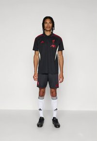 Černý sportovní dres Liverpool FC, skládající se z polokošile s červenými akcenty, odpovídajících kraťasů a bílých ponožek s černými pruhy.